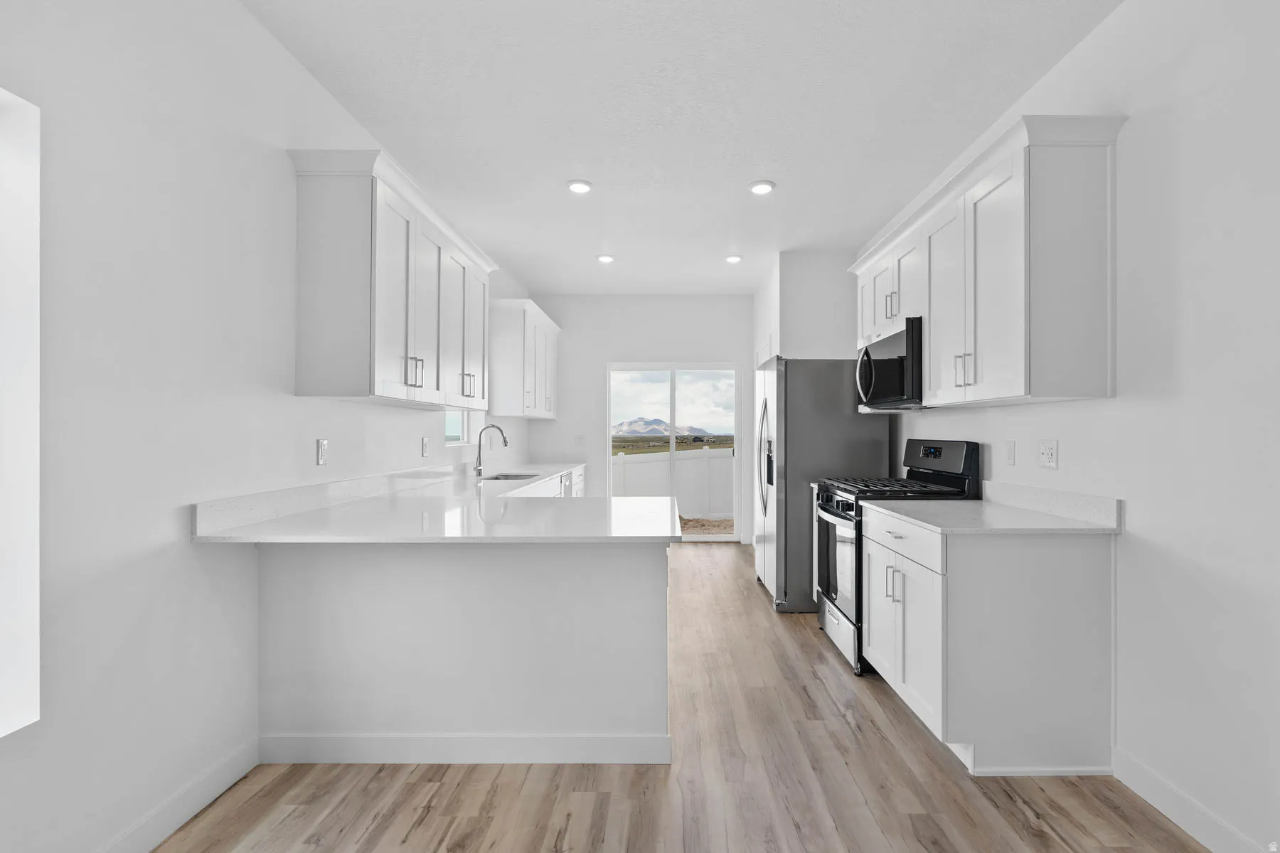 Modern kitchen featuring white shaker cabinetry, light-toned countertops, and wood-finish flooring