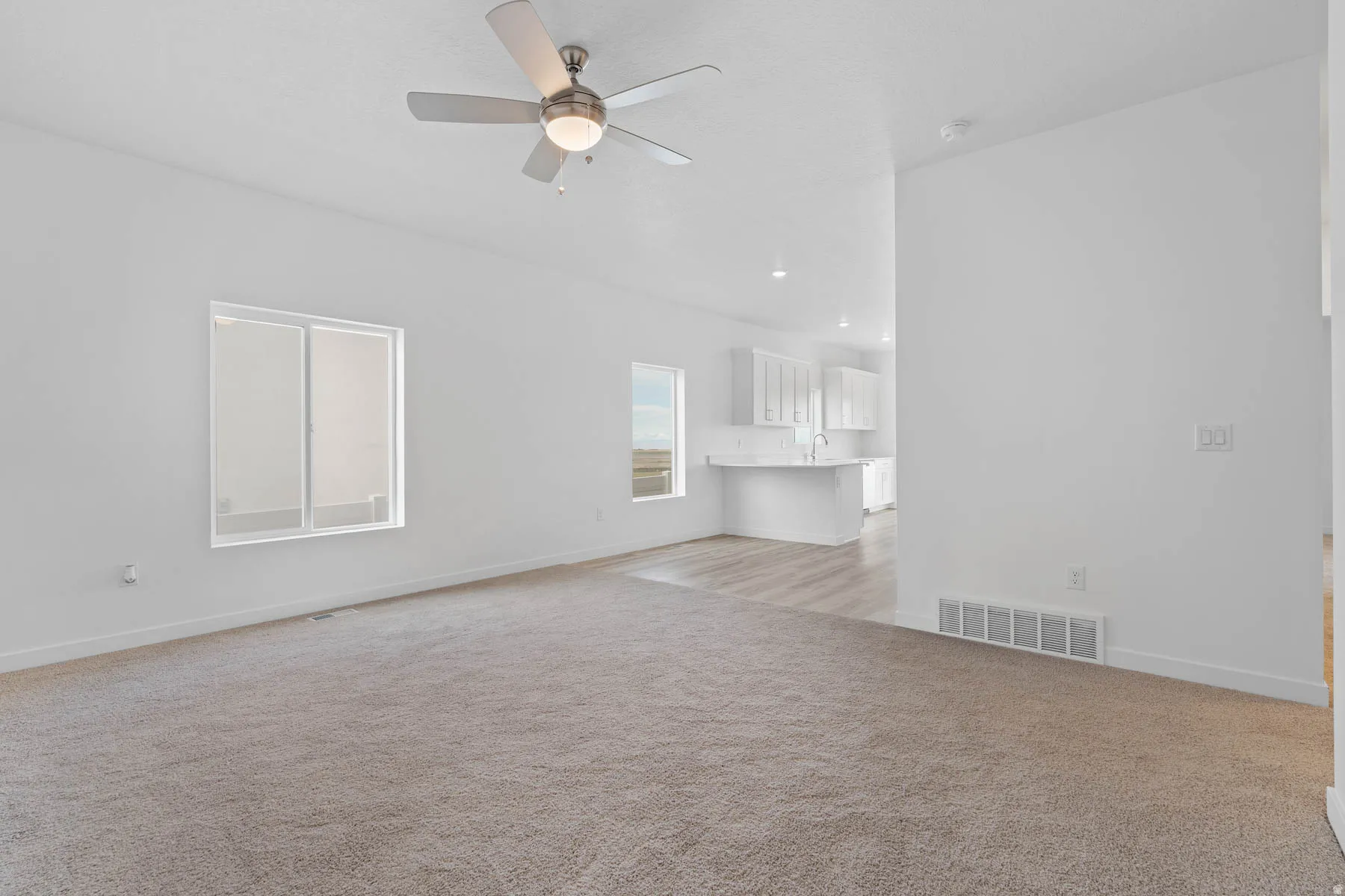 Spacious living area featuring neutral carpeting, a ceiling fan with integrated lighting, and multiple windows