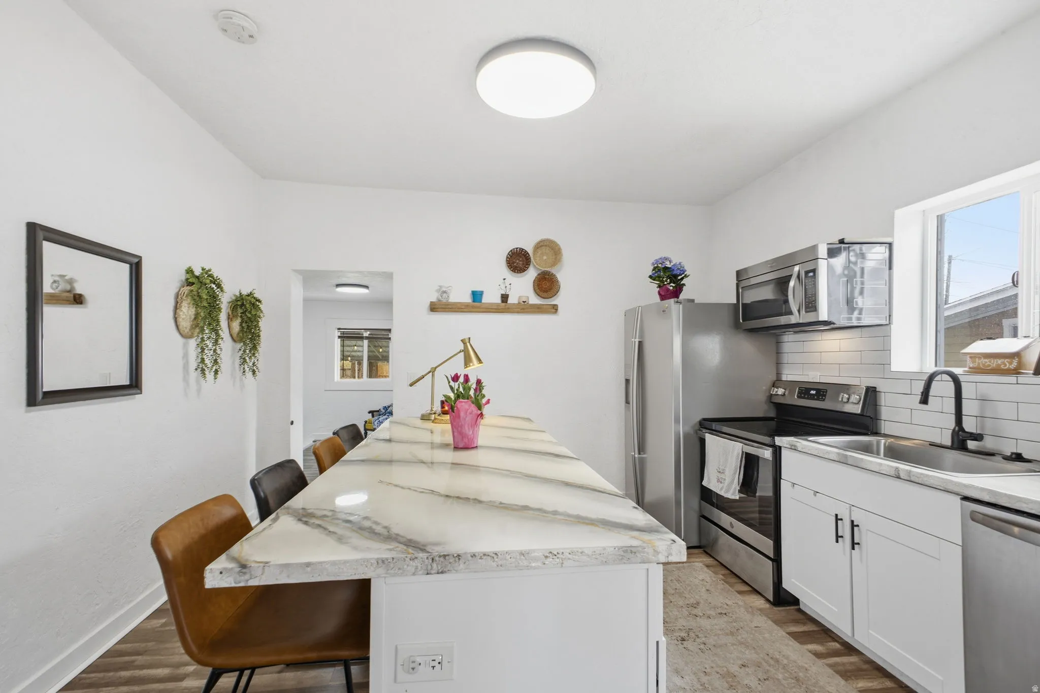 Kitchen with a kitchen bar, stainless steel appliances, decorative backsplash, dark wood-type flooring, and white cabinets