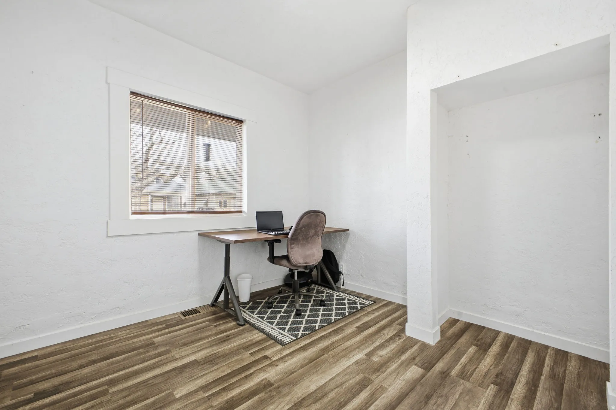 Office space with a textured wall, wood finished floors, and lofted ceiling