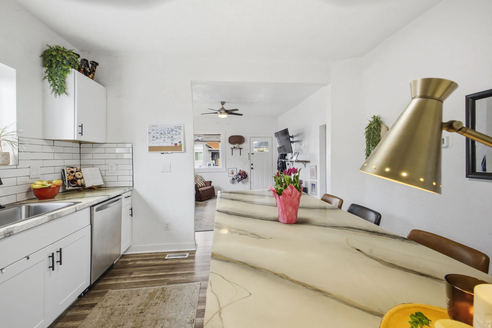 Kitchen with white cabinets, light countertops, dark wood-style floors, dishwasher, and decorative backsplash