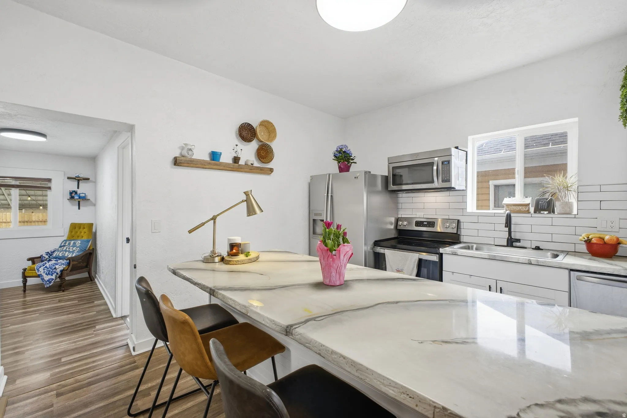 Kitchen featuring a breakfast bar, light stone countertops, decorative backsplash, white cabinets, and stainless steel appliances