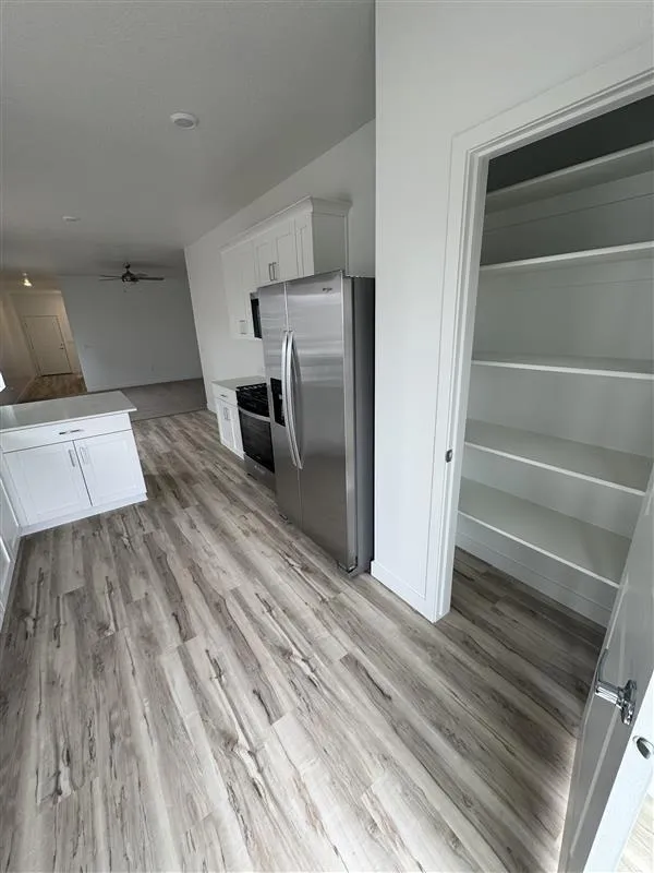 Kitchen featuring stainless steel appliances, white cabinets, light wood finished floors, and a ceiling fan