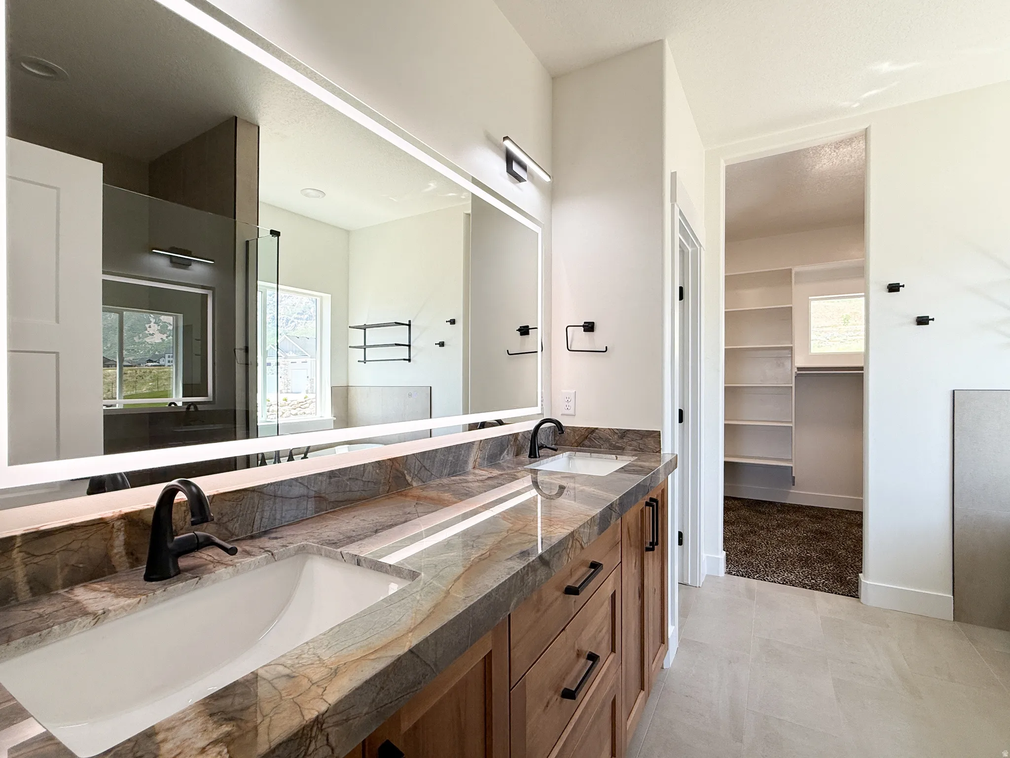 Full bath featuring double vanity, a spacious closet, light tile patterned flooring, and walk in shower
