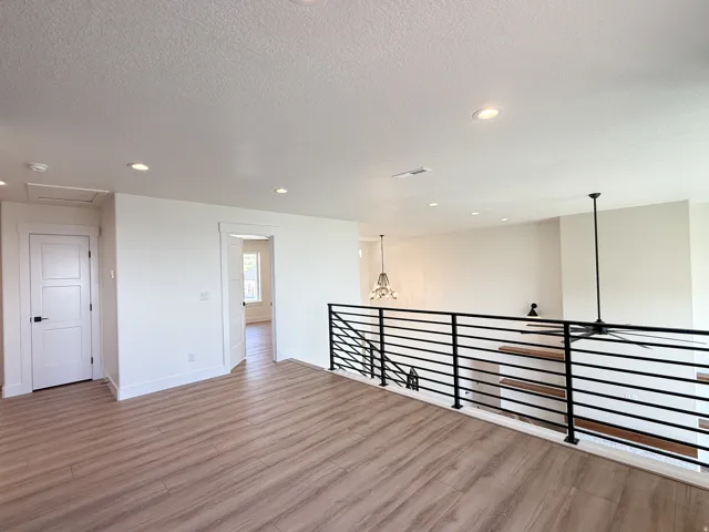 Empty room with light wood-type flooring, hanging lights, and a textured ceiling