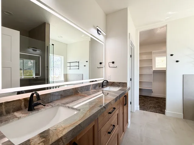 Full bath featuring double vanity, a spacious closet, light tile patterned flooring, and walk in shower