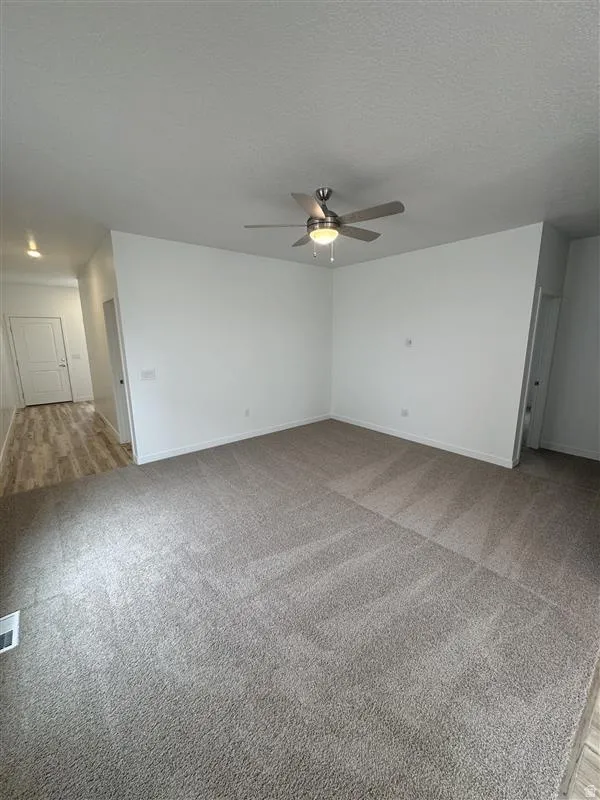 Spare room with ceiling fan, light colored carpet, and a textured ceiling