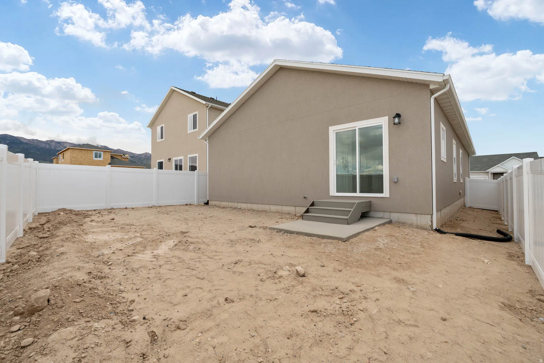 Expansive rear yard featuring a newly installed white vinyl fence, stucco exterior siding, concrete patio, and sliding glass door access