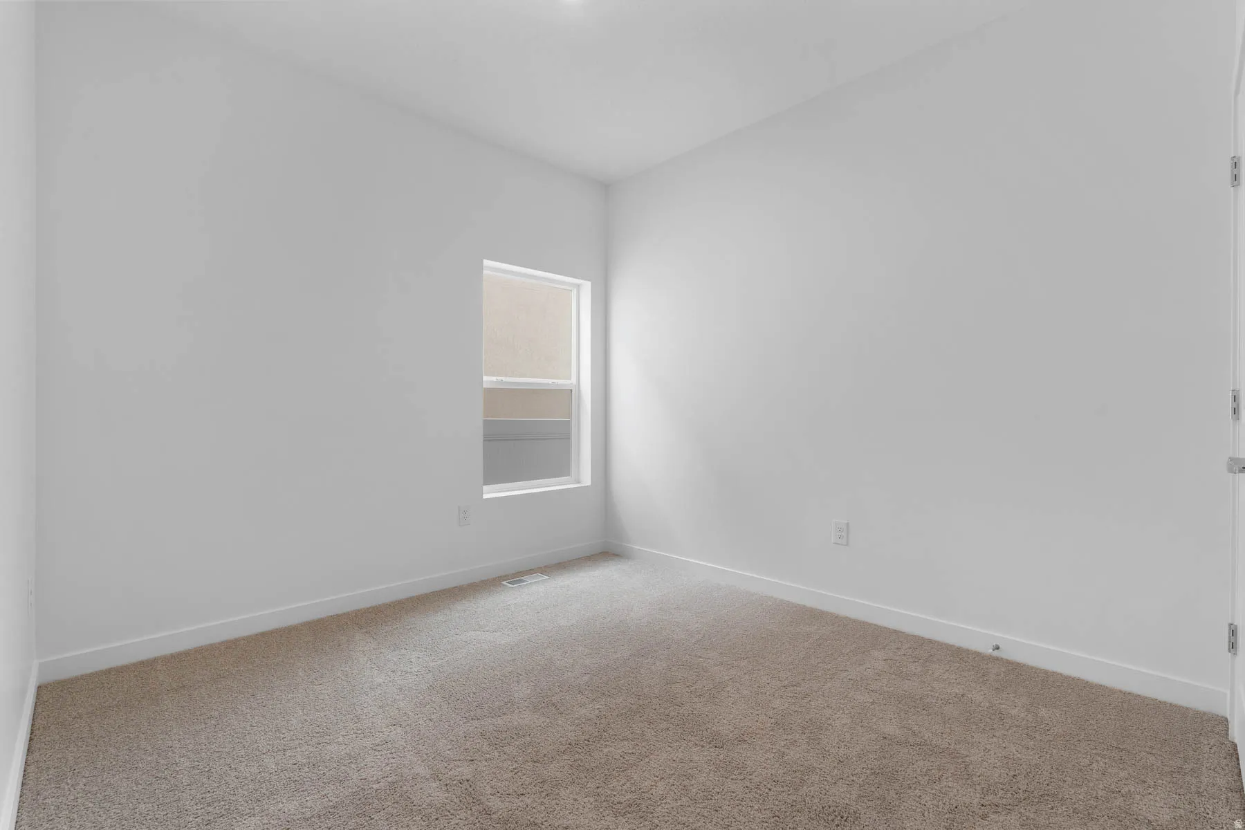 Bright room with a neutral color palette, featuring plush carpeting, a single window, and white baseboards