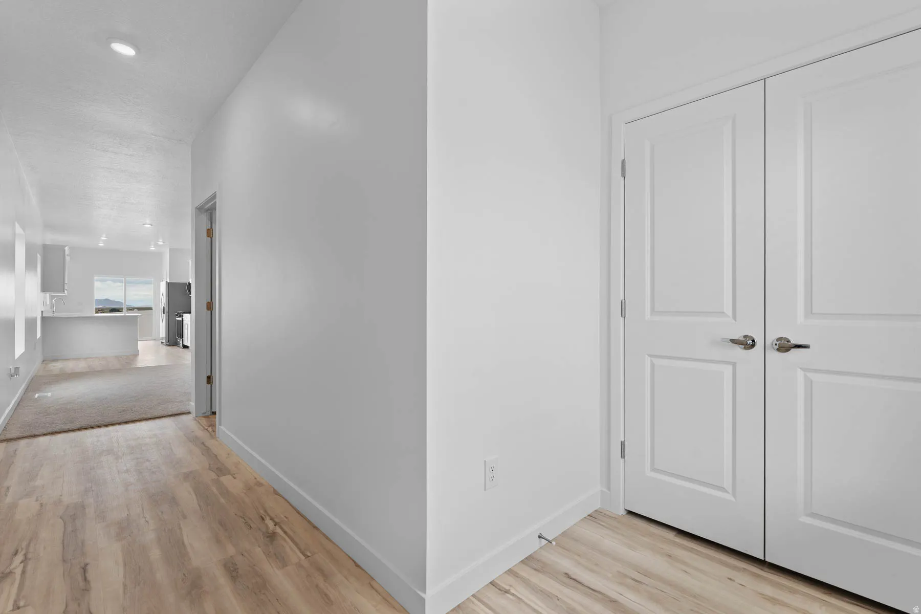 Recessed lighting illuminates the hallway featuring wood-finish flooring and white walls