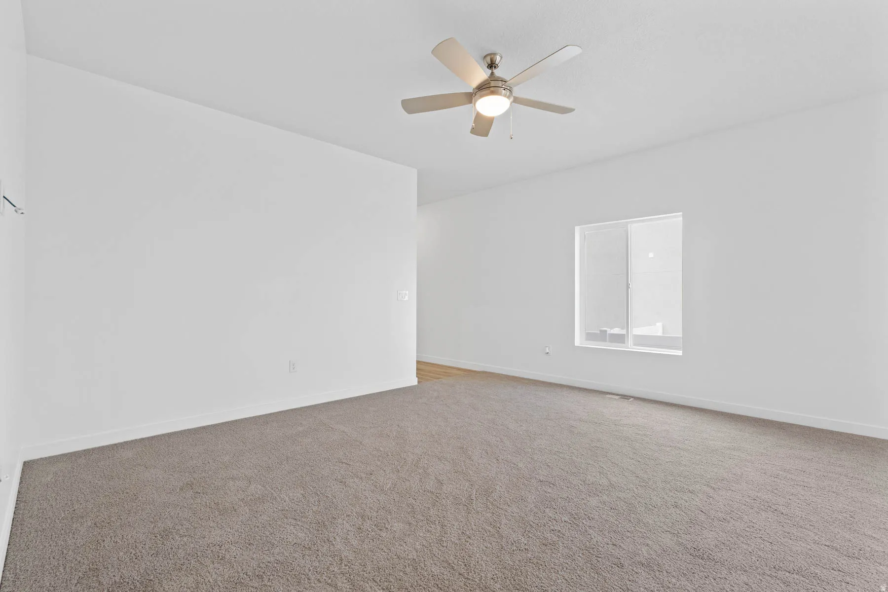 Spacious room featuring neutral carpet flooring, a ceiling fan with integrated lighting, and a large window