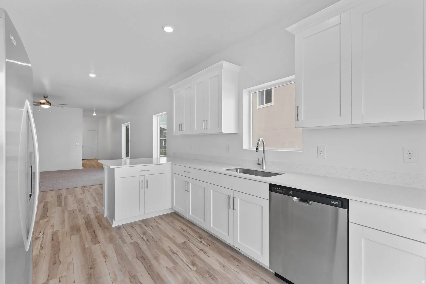 Modern kitchen featuring white shaker cabinetry, stainless steel appliances, light-toned countertops, and wood-finish flooring