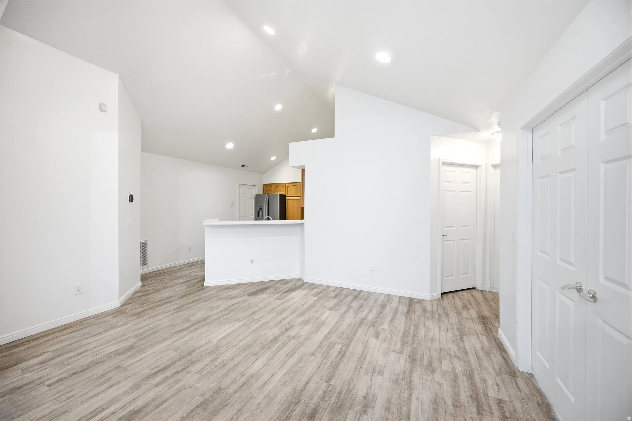 Unfurnished living room featuring light wood-style floors, vaulted ceiling, and recessed lighting