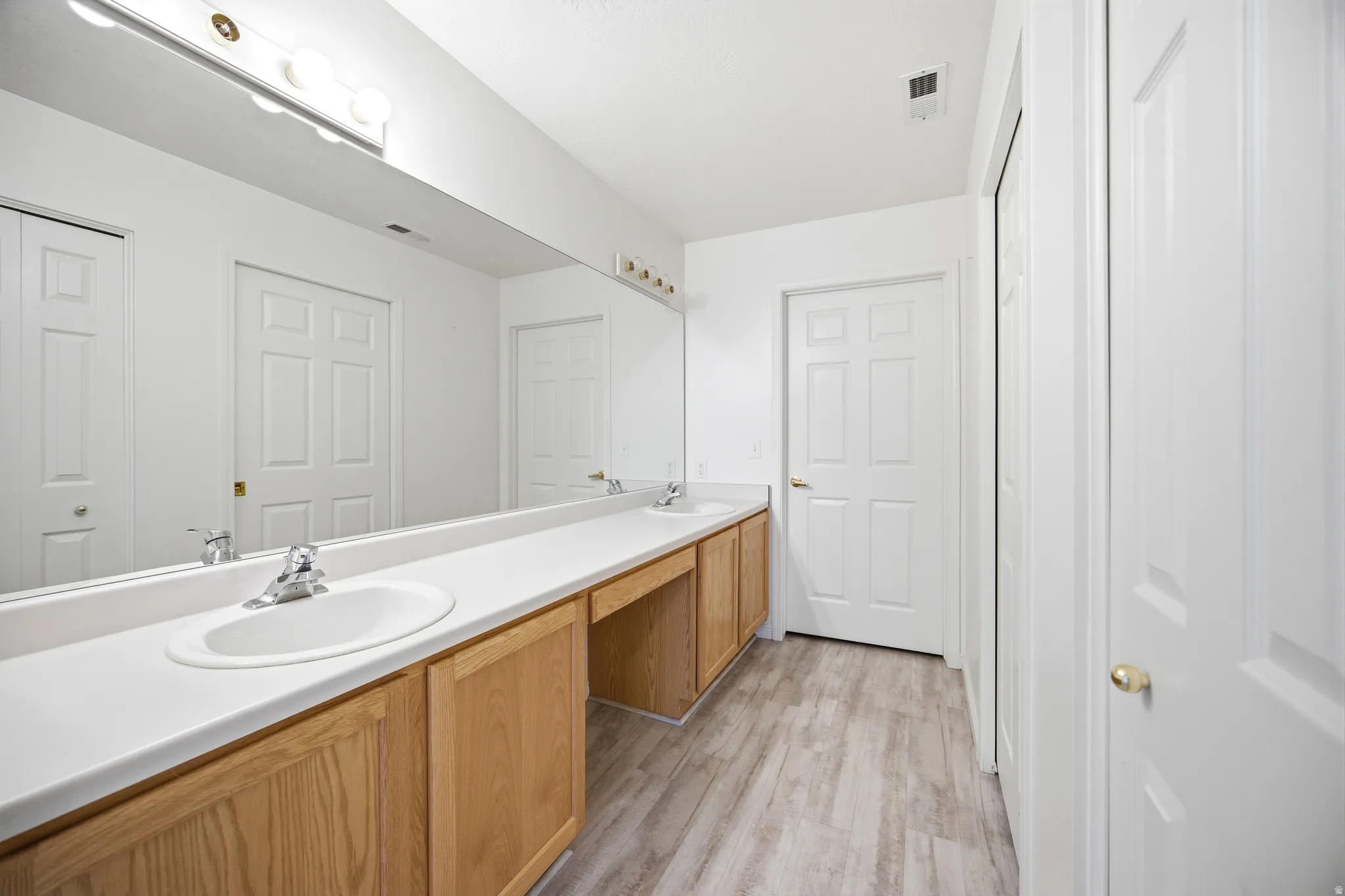 Full bath with double vanity and light wood finished floors
