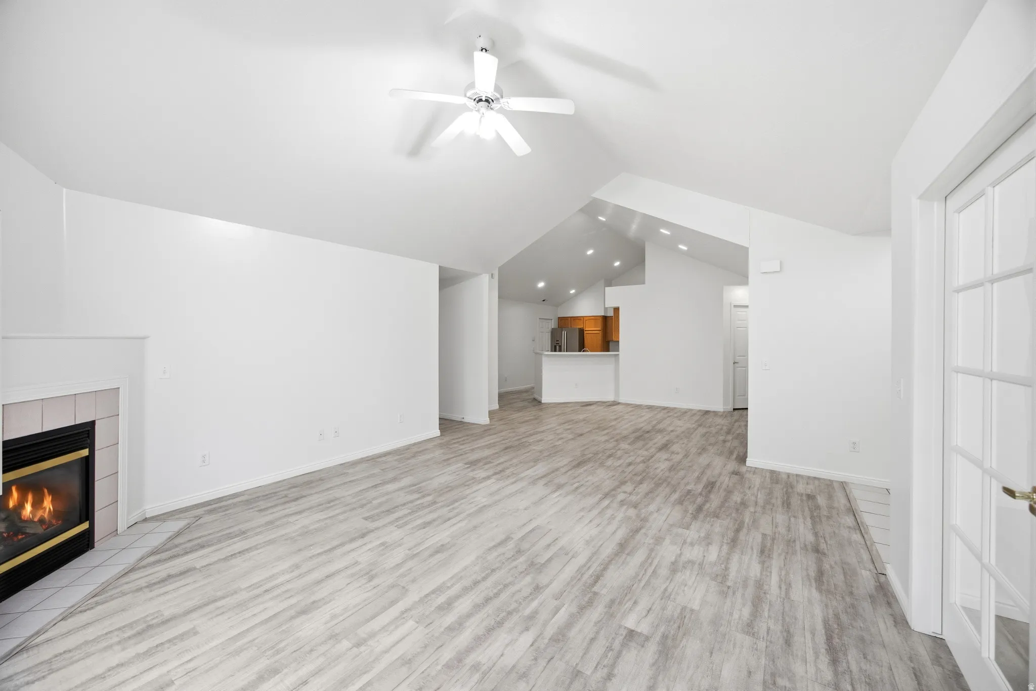 Unfurnished living room featuring a tiled fireplace, a ceiling fan, and light wood-type flooring
