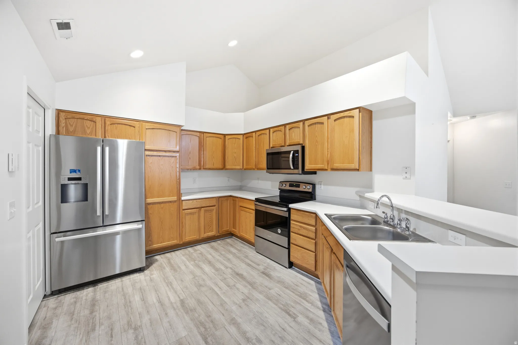 Kitchen with stainless steel appliances, a peninsula, light countertops, lofted ceiling, and light wood-style flooring