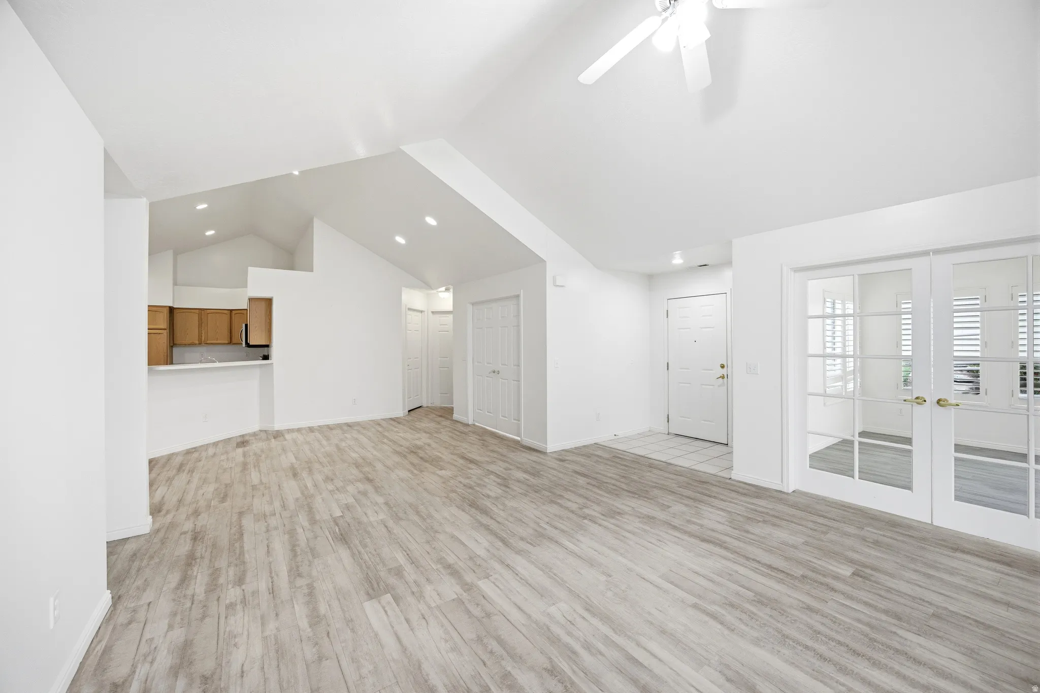 Unfurnished living room featuring french doors, a ceiling fan, a high ceiling, light wood-style floors, and recessed lighting