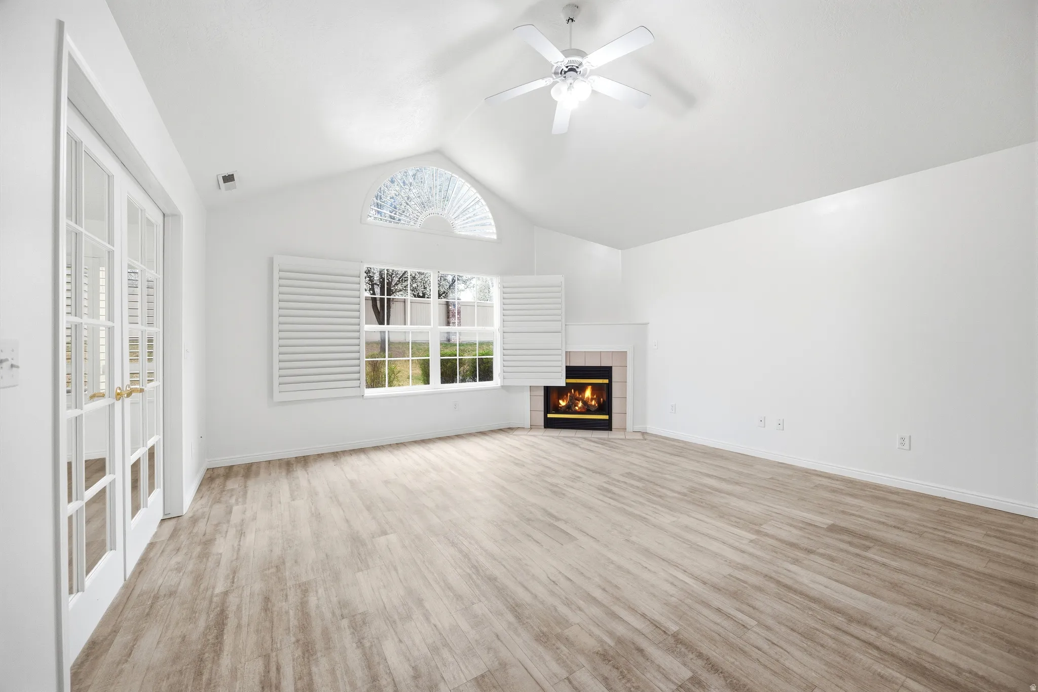 Unfurnished living room with ceiling fan, light wood-style floors, a tiled fireplace, and a high ceiling