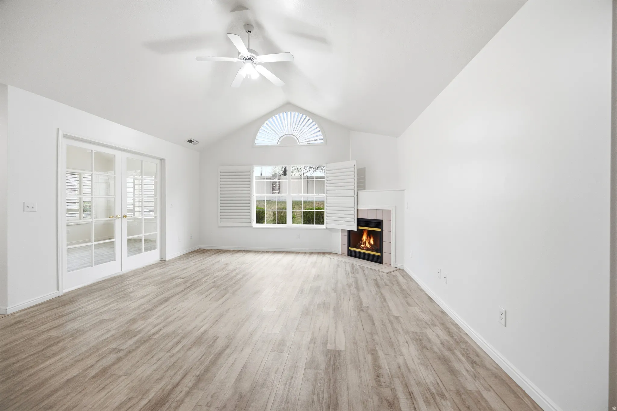 Unfurnished living room featuring light wood-style floors, a tile fireplace, a ceiling fan, and a high ceiling
