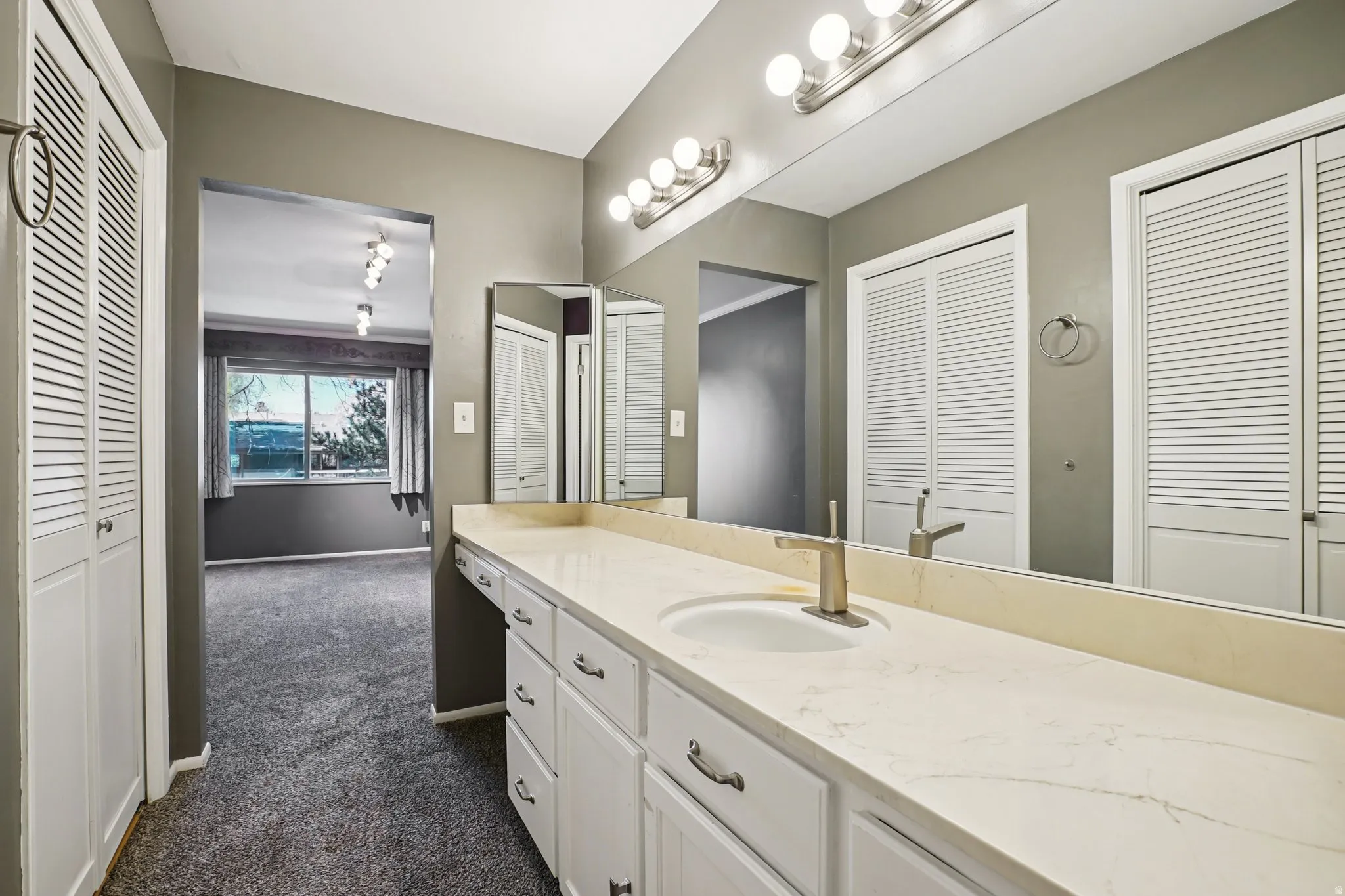 Bathroom with a closet, vanity, and dark colored carpet