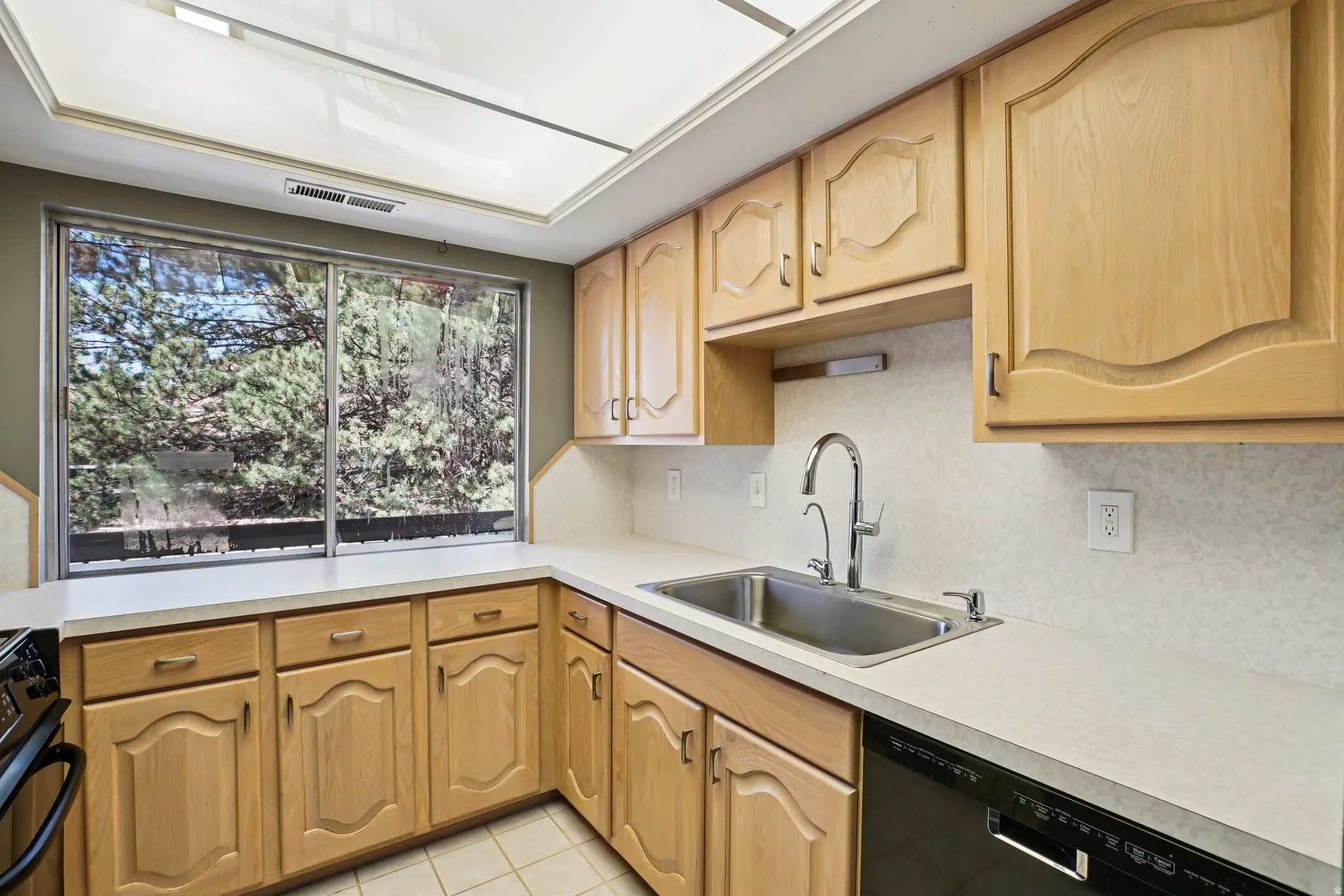 Kitchen with black appliances, light countertops, light tile patterned floors, light wood finish cabinets, and tasteful backsplash