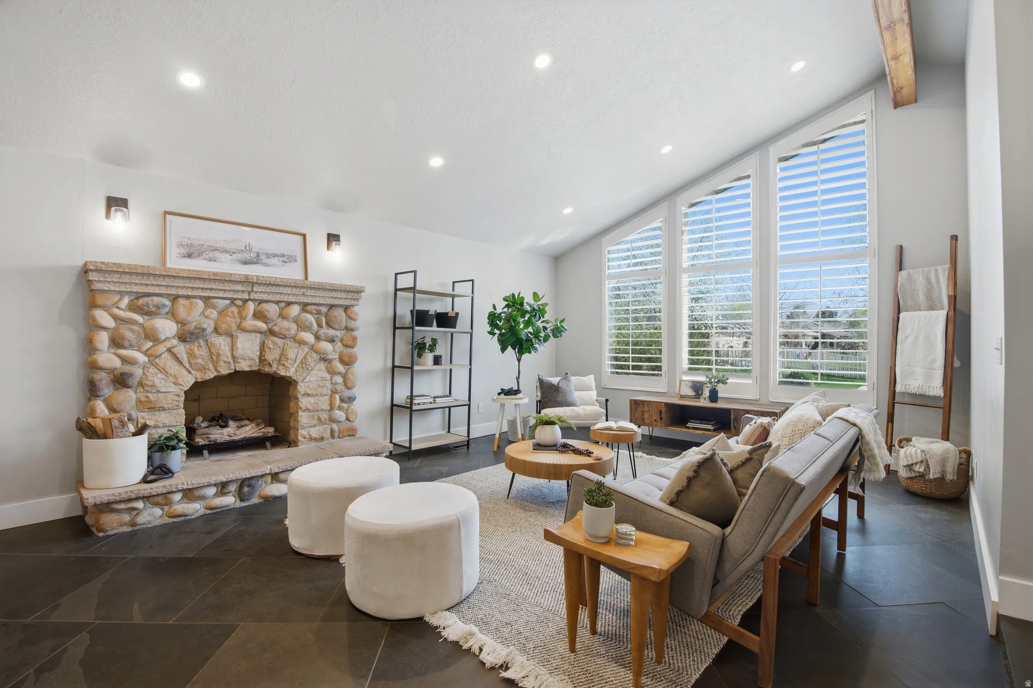 Living room with vaulted ceiling with beams, a stone fireplace, and recessed lighting