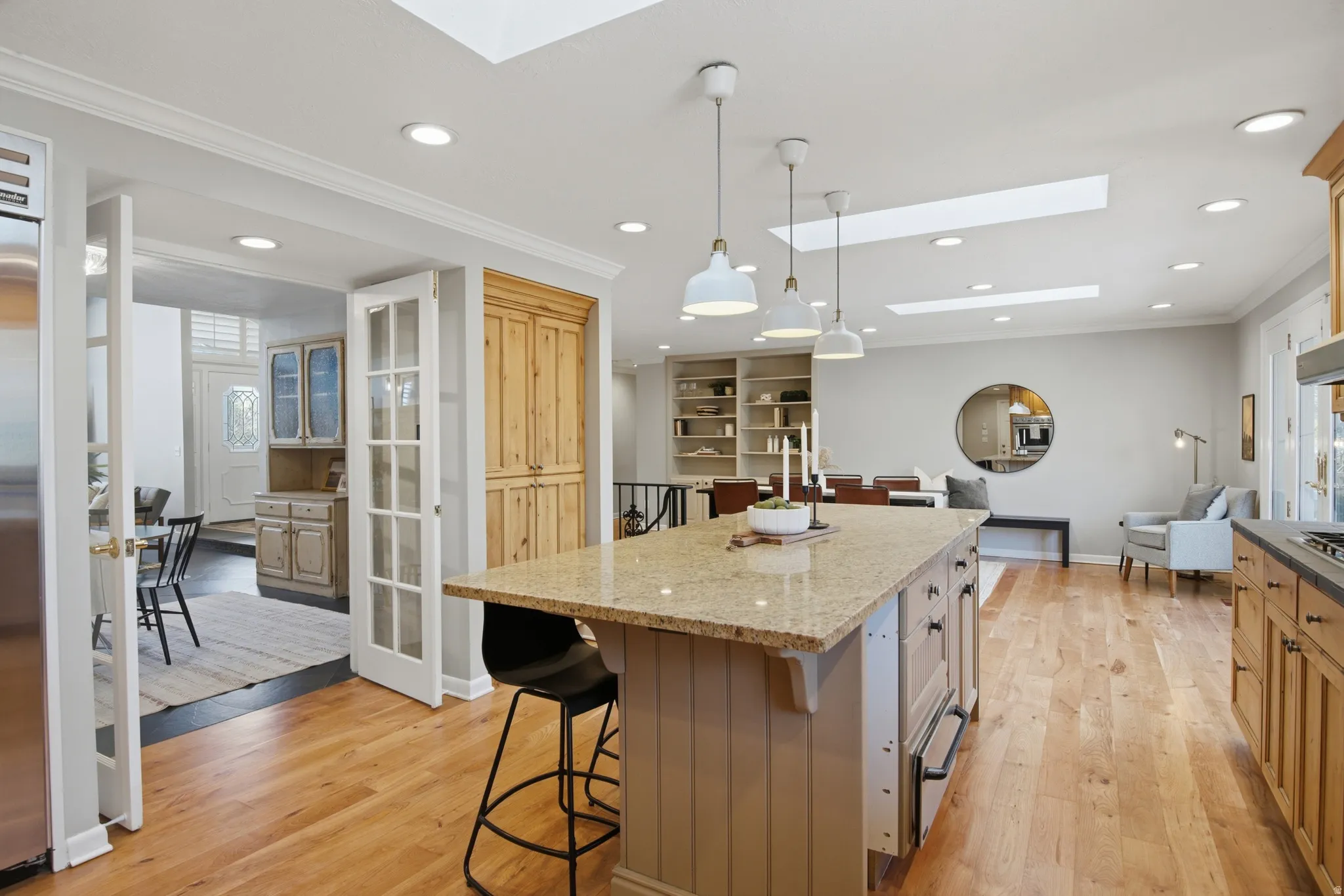 Kitchen with a skylight, a kitchen bar, crown molding, decorative light fixtures, and light stone counters