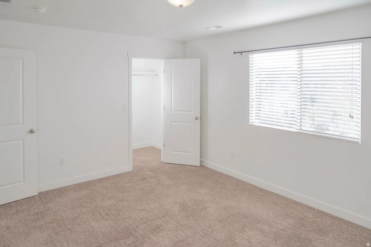 Unfurnished bedroom with a walk in closet and light colored carpet