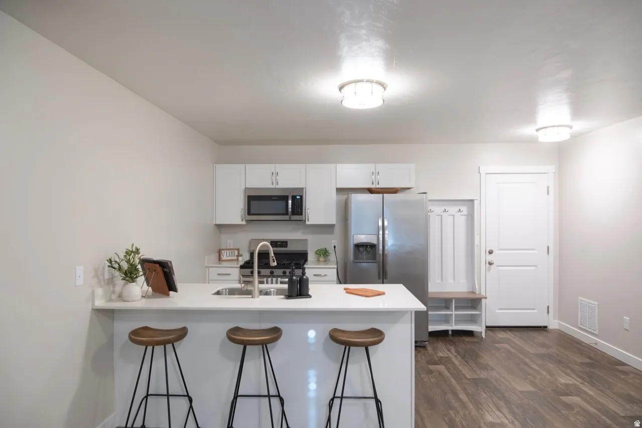 Kitchen with a kitchen breakfast bar, a peninsula, white cabinetry, stainless steel appliances, and dark wood finished floors
