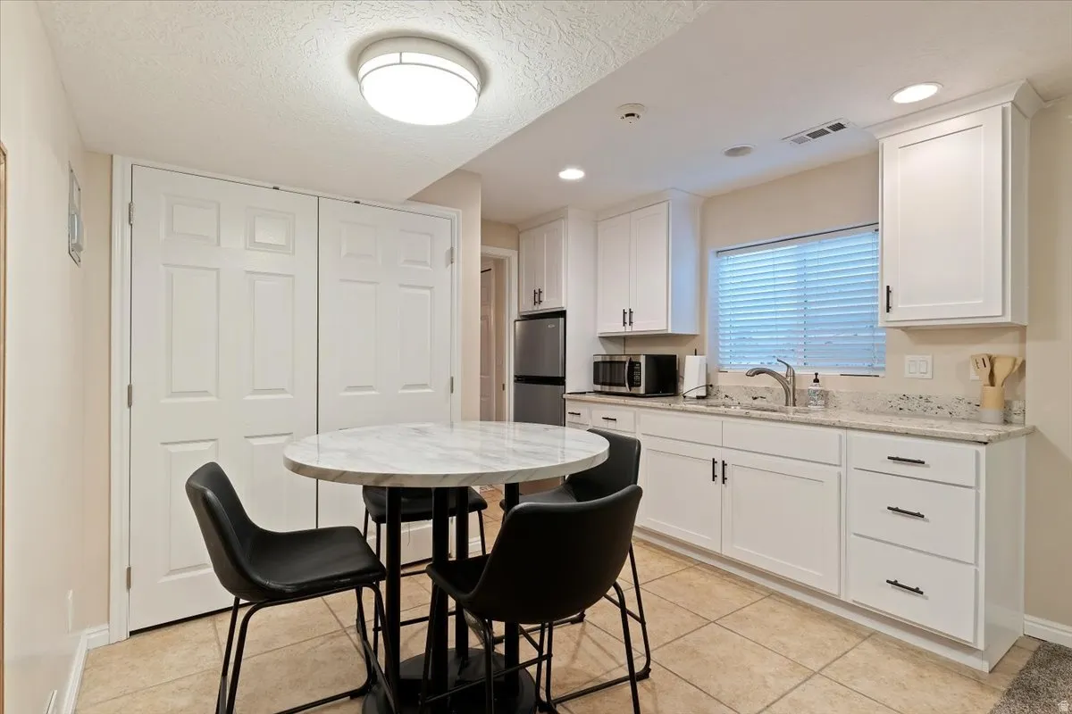 Kitchen with white cabinetry, stainless steel appliances, light stone counters, light tile patterned floors, and a textured ceiling