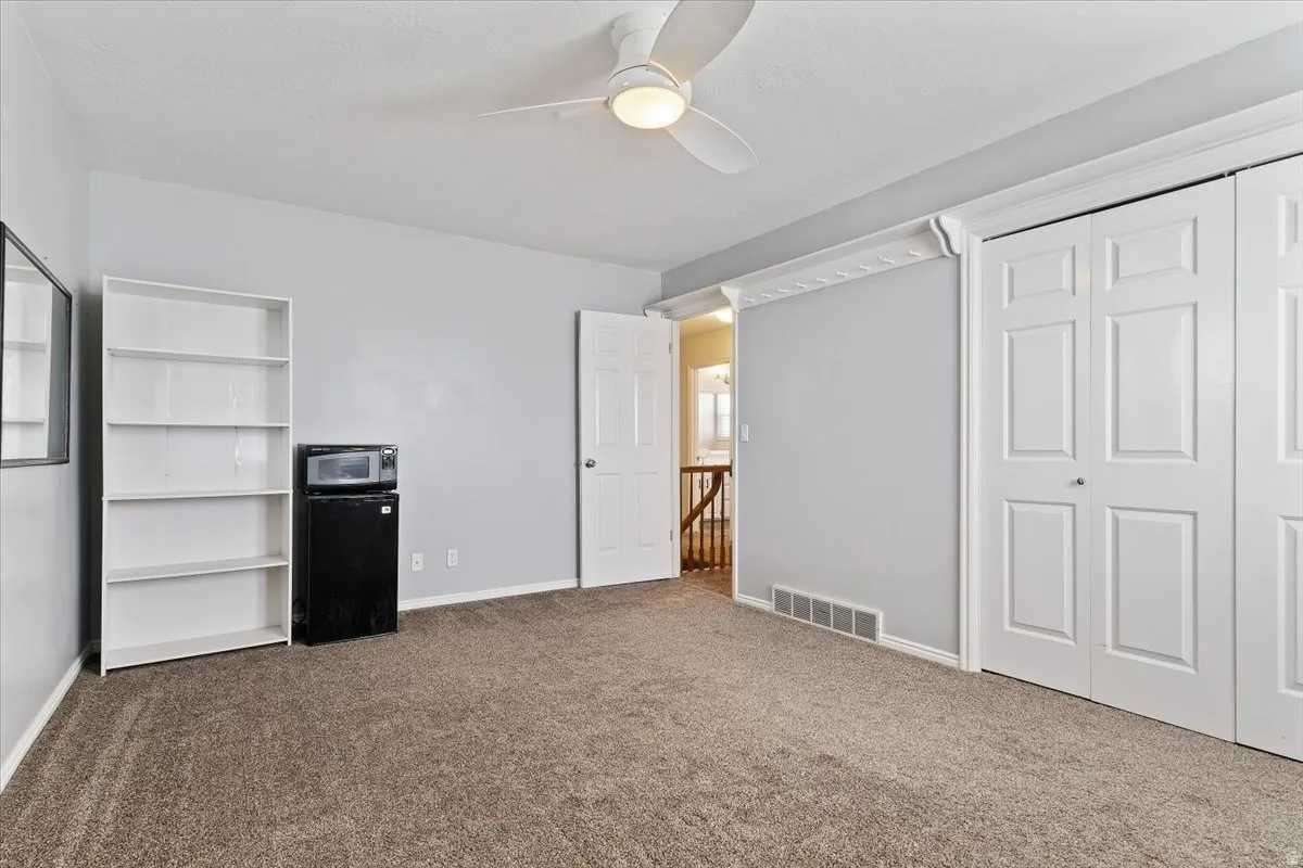 Unfurnished bedroom with dark colored carpet, a closet, ceiling fan, and black refrigerator
