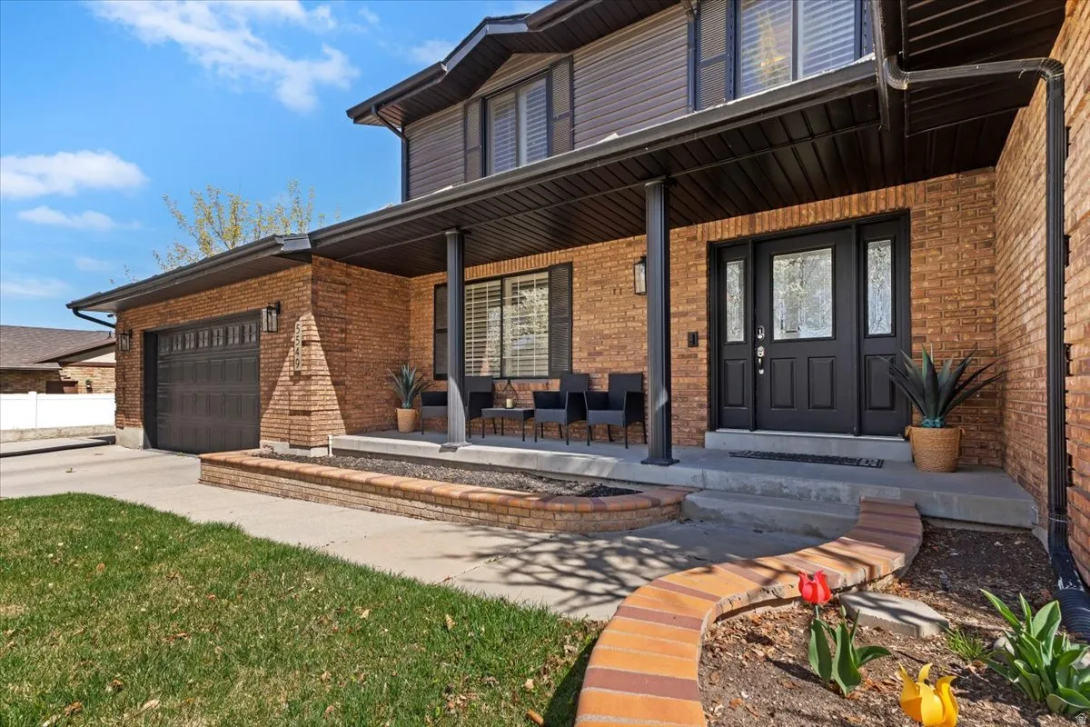 Doorway to property with covered porch, brick siding, an attached garage, and driveway