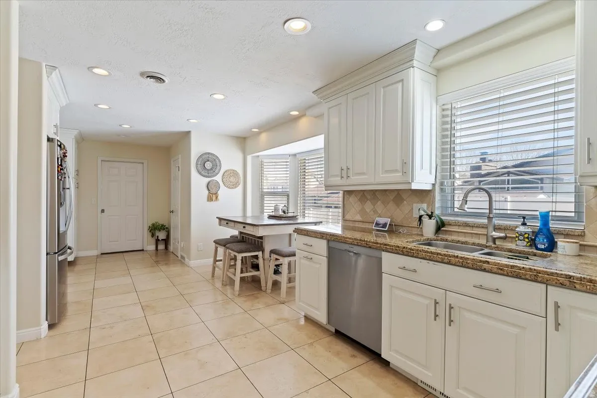Kitchen featuring white cabinets, light tile patterned floors, stainless steel appliances, recessed lighting, and decorative backsplash