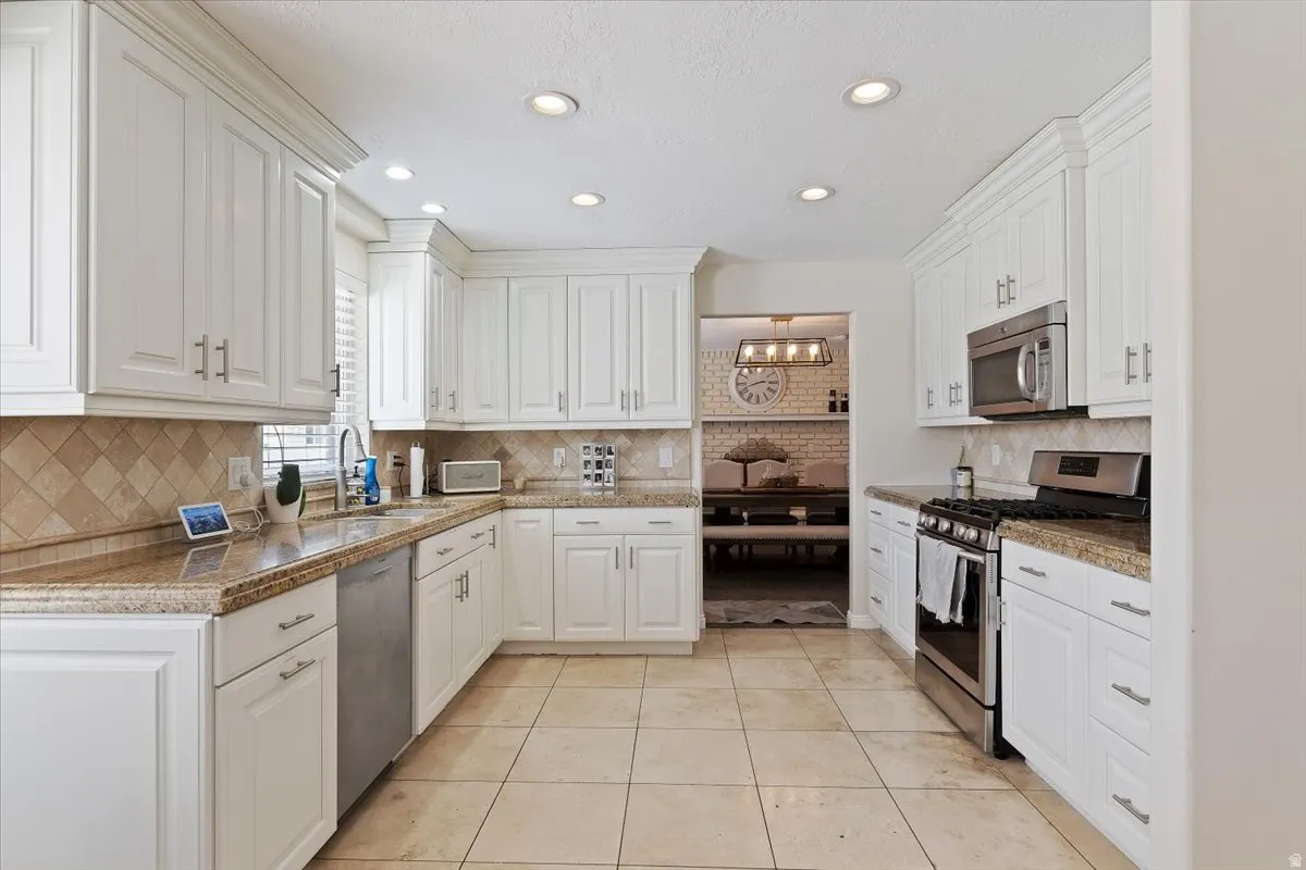 Kitchen with stainless steel appliances, white cabinetry, light tile patterned flooring, and recessed lighting
