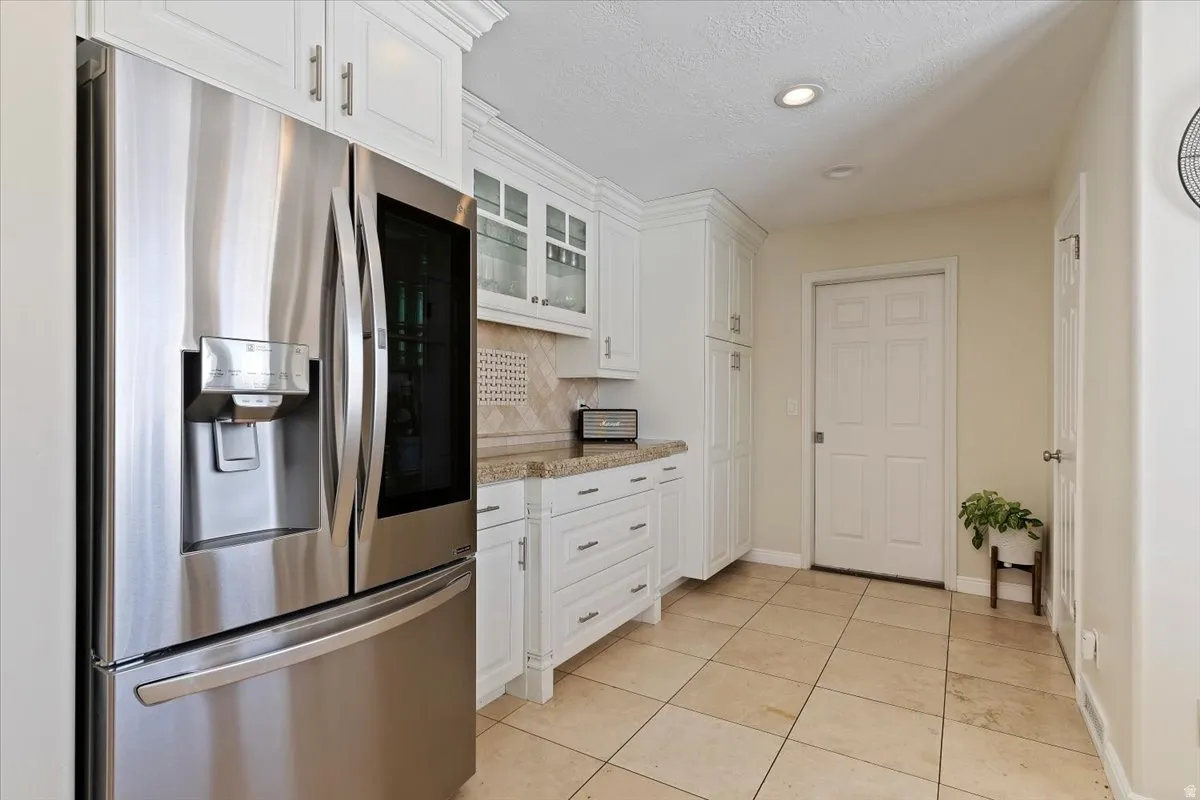 Kitchen with stainless steel refrigerator with ice dispenser, white cabinets, tasteful backsplash, glass fronted cabinets, and recessed lighting