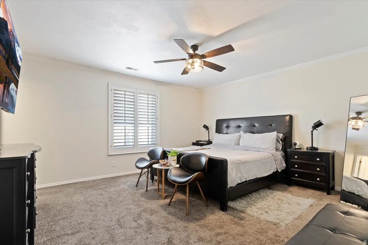Bedroom featuring light carpet, a ceiling fan, and crown molding