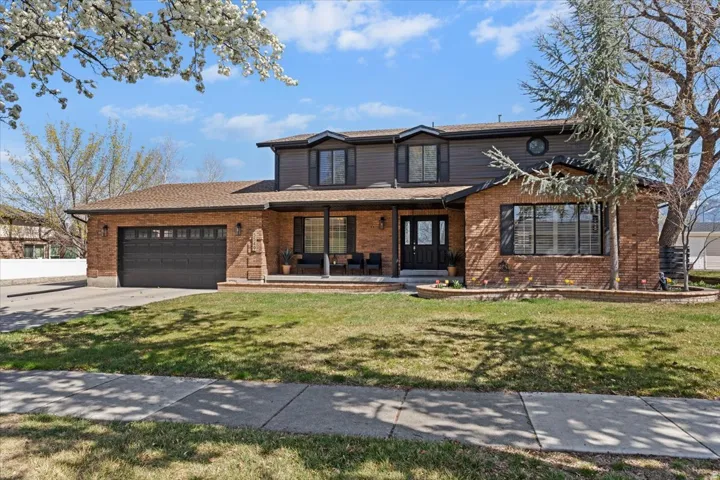 Traditional home with a porch, brick siding, a front yard, driveway, and an attached garage