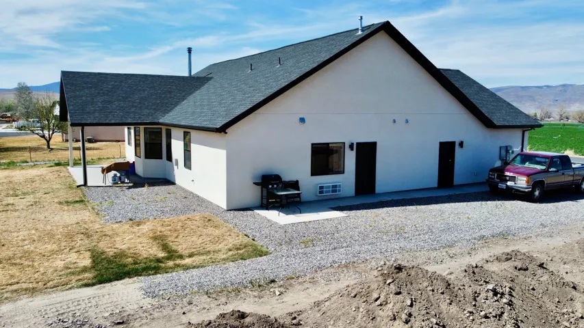 View of side of property with a mountain view, a shingled roof, a patio, and stucco siding