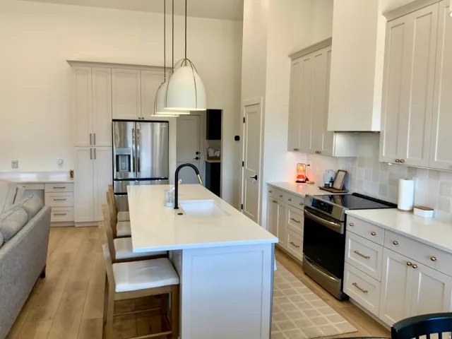 Kitchen with stainless steel appliances, an island with sink, white cabinets, and a high ceiling