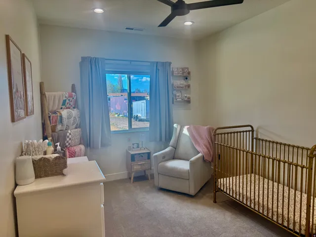 Carpeted bedroom with a crib, a ceiling fan, and recessed lighting
