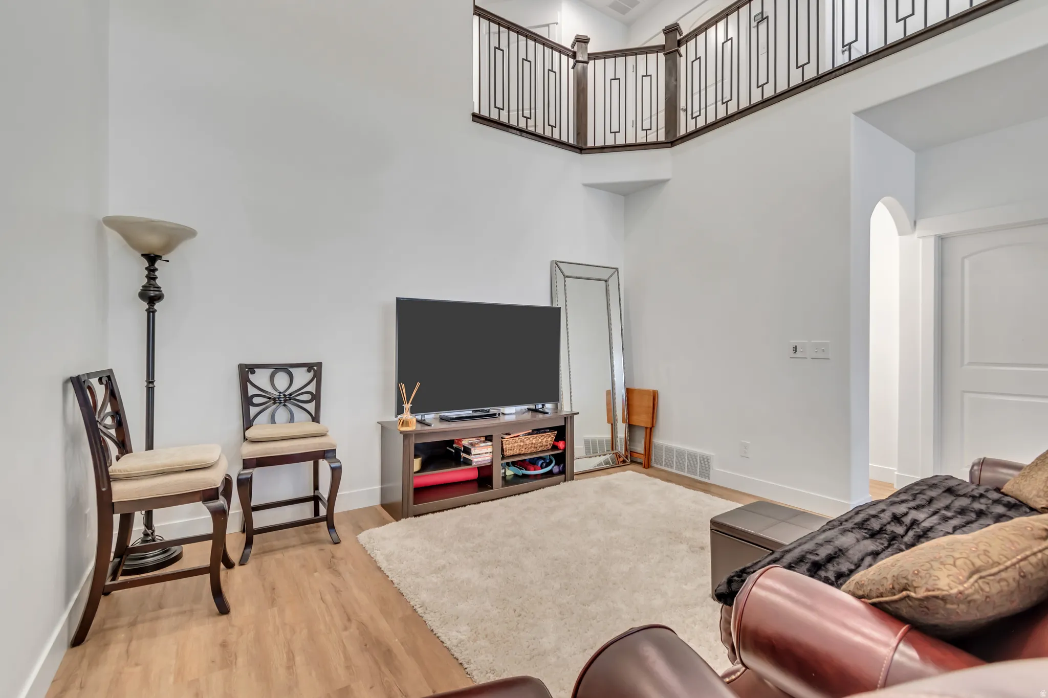 Living area with arched walkways, light wood-style floors, and a high ceiling