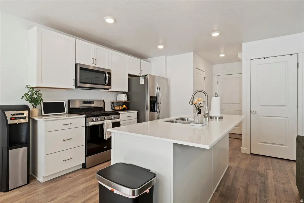 Kitchen with stainless steel appliances, light wood-type flooring, a kitchen island with sink, white cabinetry, and recessed lighting