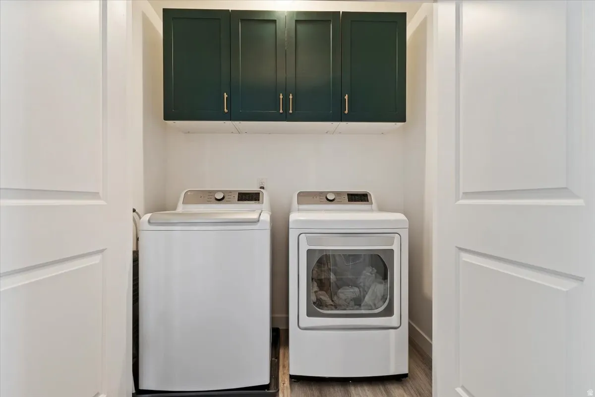 Laundry room featuring separate washer and dryer, cabinet space, and wood finished floors