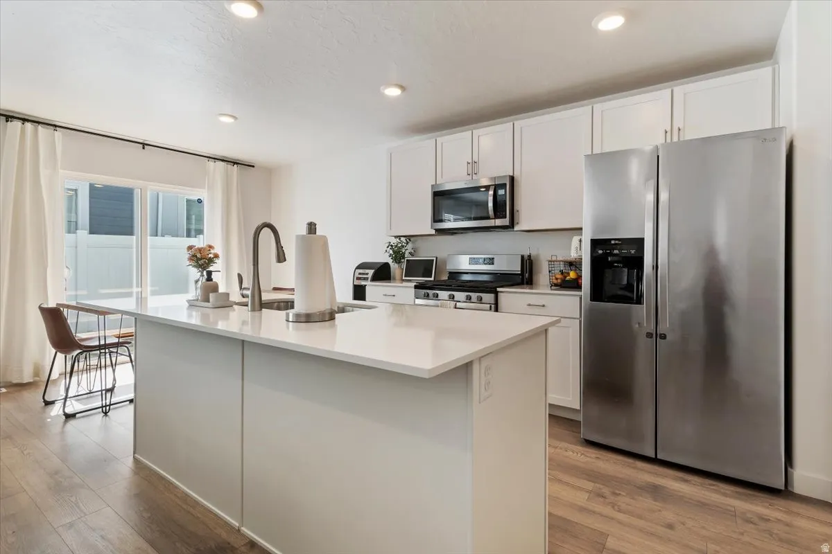Kitchen featuring stainless steel appliances, white cabinetry, a kitchen island with sink, light wood finished floors, and recessed lighting