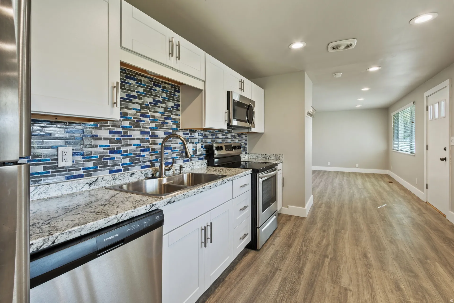 Kitchen featuring stainless steel appliances, white cabinetry, recessed lighting, dark wood-type flooring, and light stone counters
