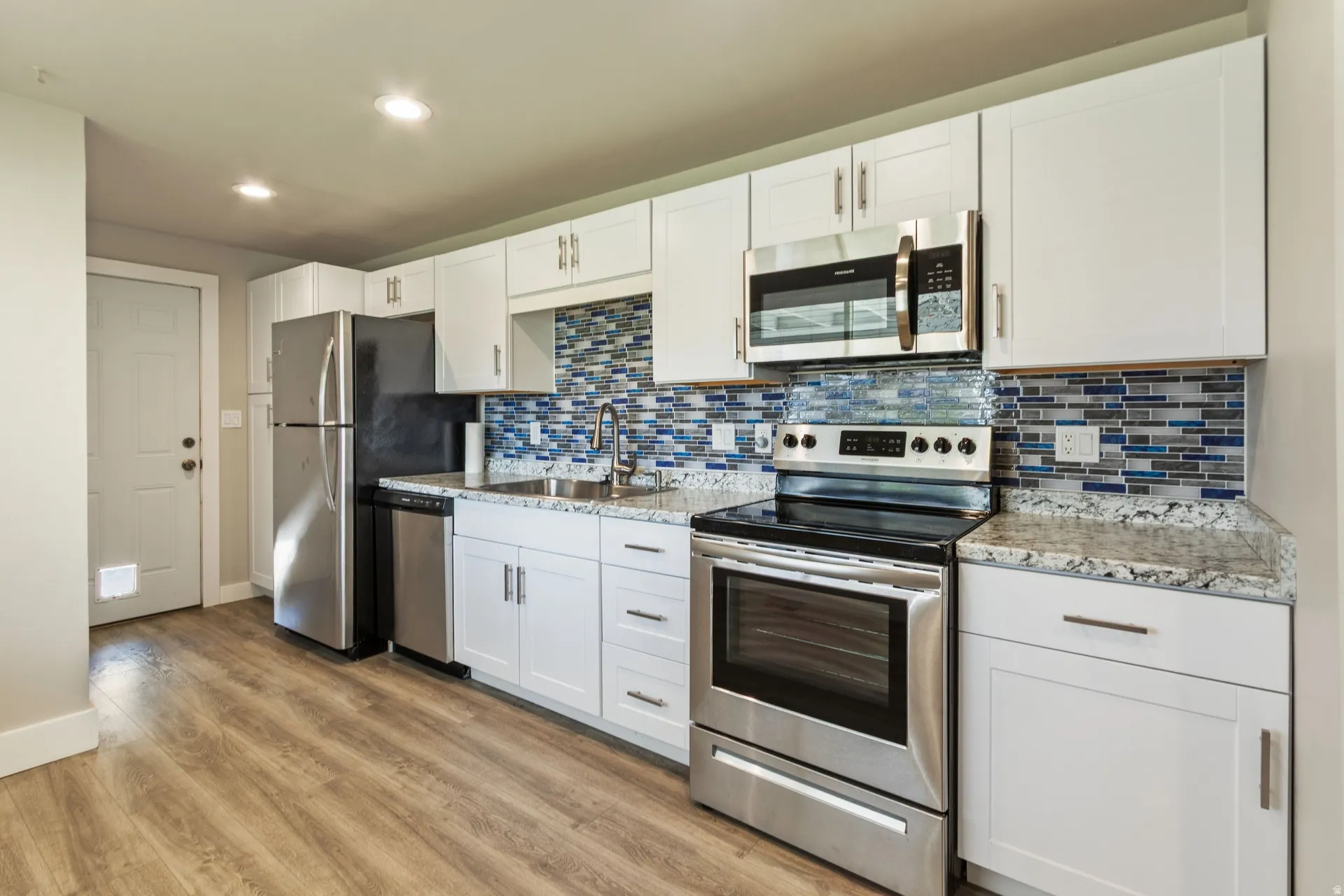 Kitchen with stainless steel appliances, white cabinets, light stone countertops, light wood finished floors, and recessed lighting