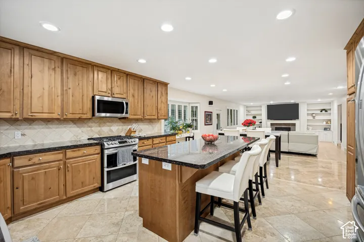 Kitchen featuring wood cabinets, stainless steel appliances, a large island with granite countertop, and Travertine tile flooring