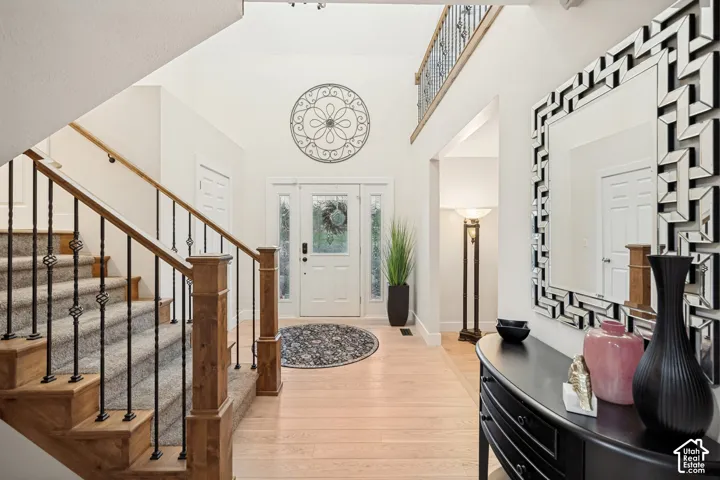 Vaulted ceiling entry featuring a two-story foyer, hardwood flooring, and a staircase