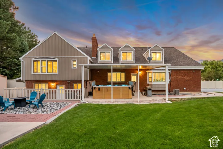 Expansive backyard featuring a manicured lawn, fire pit, covered patio area, and swim spa
