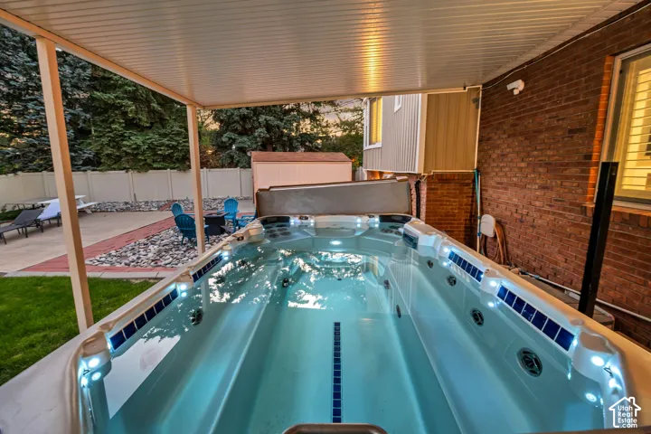Covered swim spa with integrated lighting, brick exterior, and a paved patio area